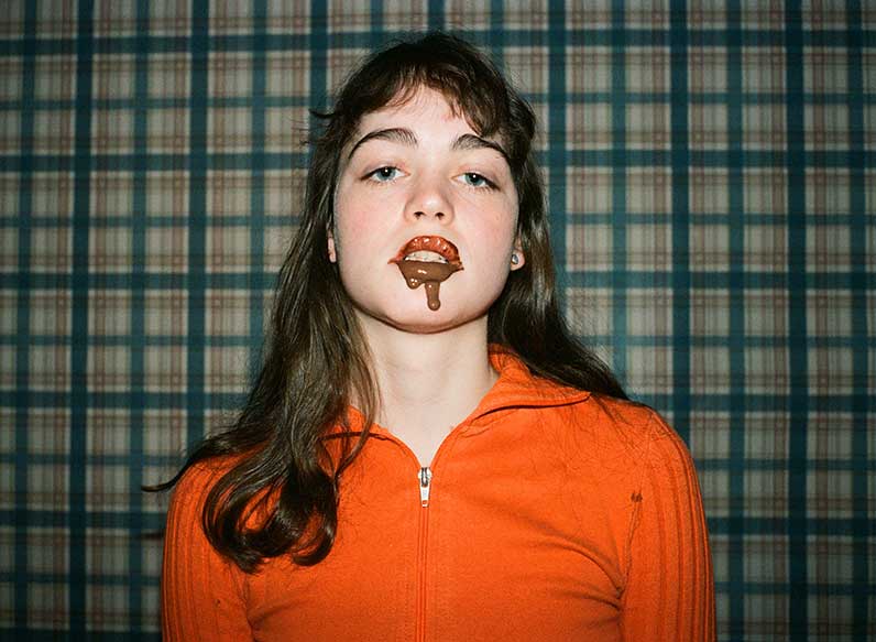 ragazza con maglia arancione con cioccolato sulla bocca